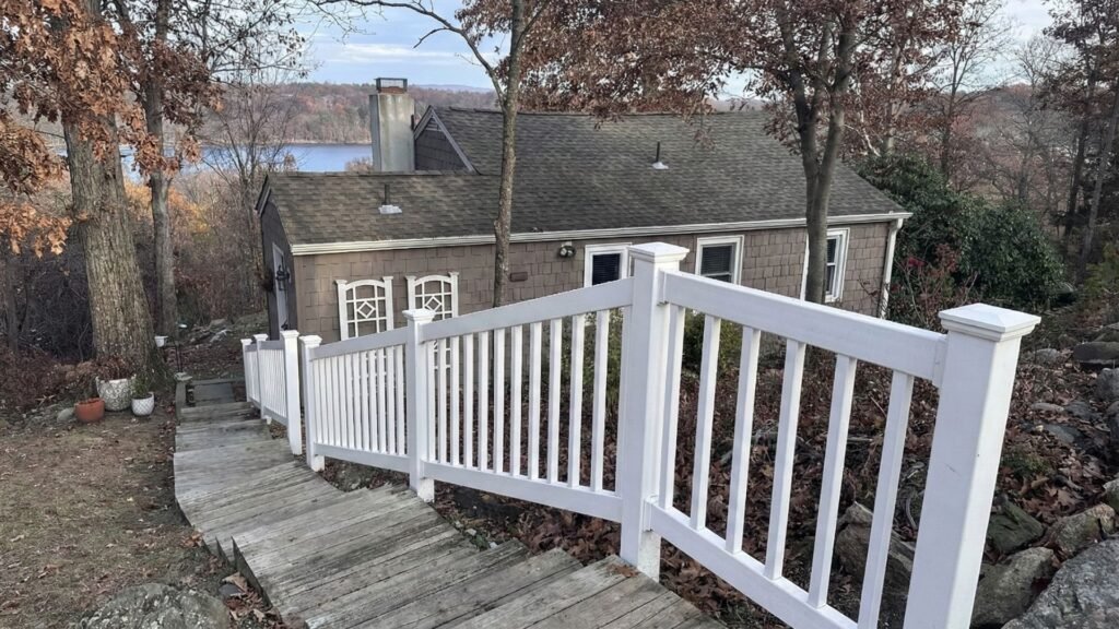 White wooden deck railing with vertical balusters overlooking a lake, installed on a weathered deck in autumn