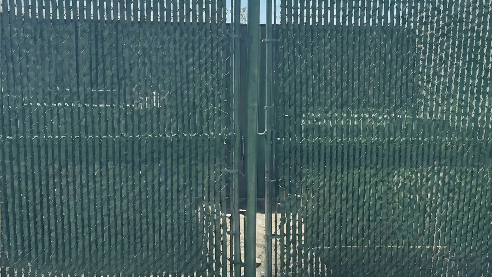 Green chain link industrial fence with privacy slats and double gate entrance on concrete surface