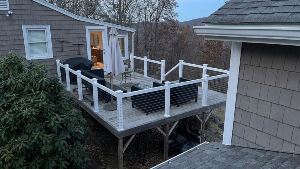 Modern white cable railing system installed on elevated deck with outdoor furniture and shingled house exterior