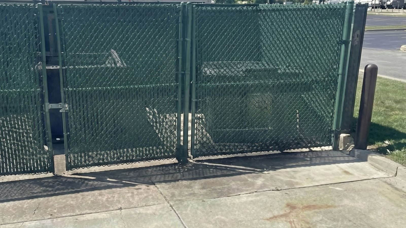 Green chain link fence gates with security latches installed on concrete pad at commercial property entrance
