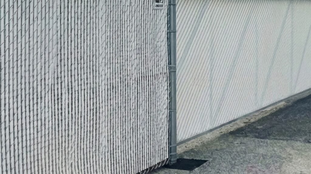 White chain link fence with privacy slats installed along concrete surface with metal posts and barbed wire