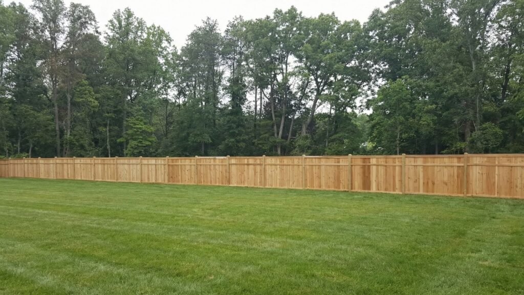New wooden privacy fence installed in residential backyard with lush green lawn and mature trees in background