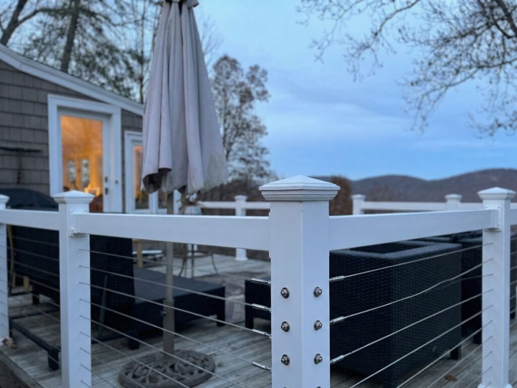 White deck railing with black cable infill panels installed on outdoor deck at dusk with house and mountains in background