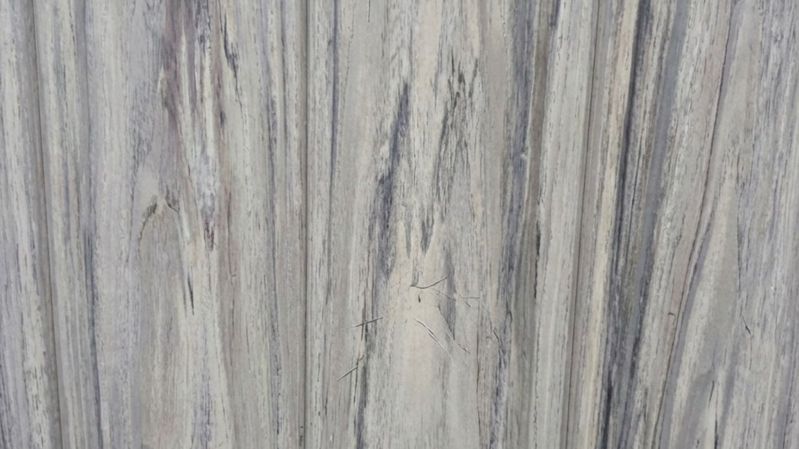 Close-up view of weathered gray vinyl fence boards showing vertical wood grain texture and natural aging patterns