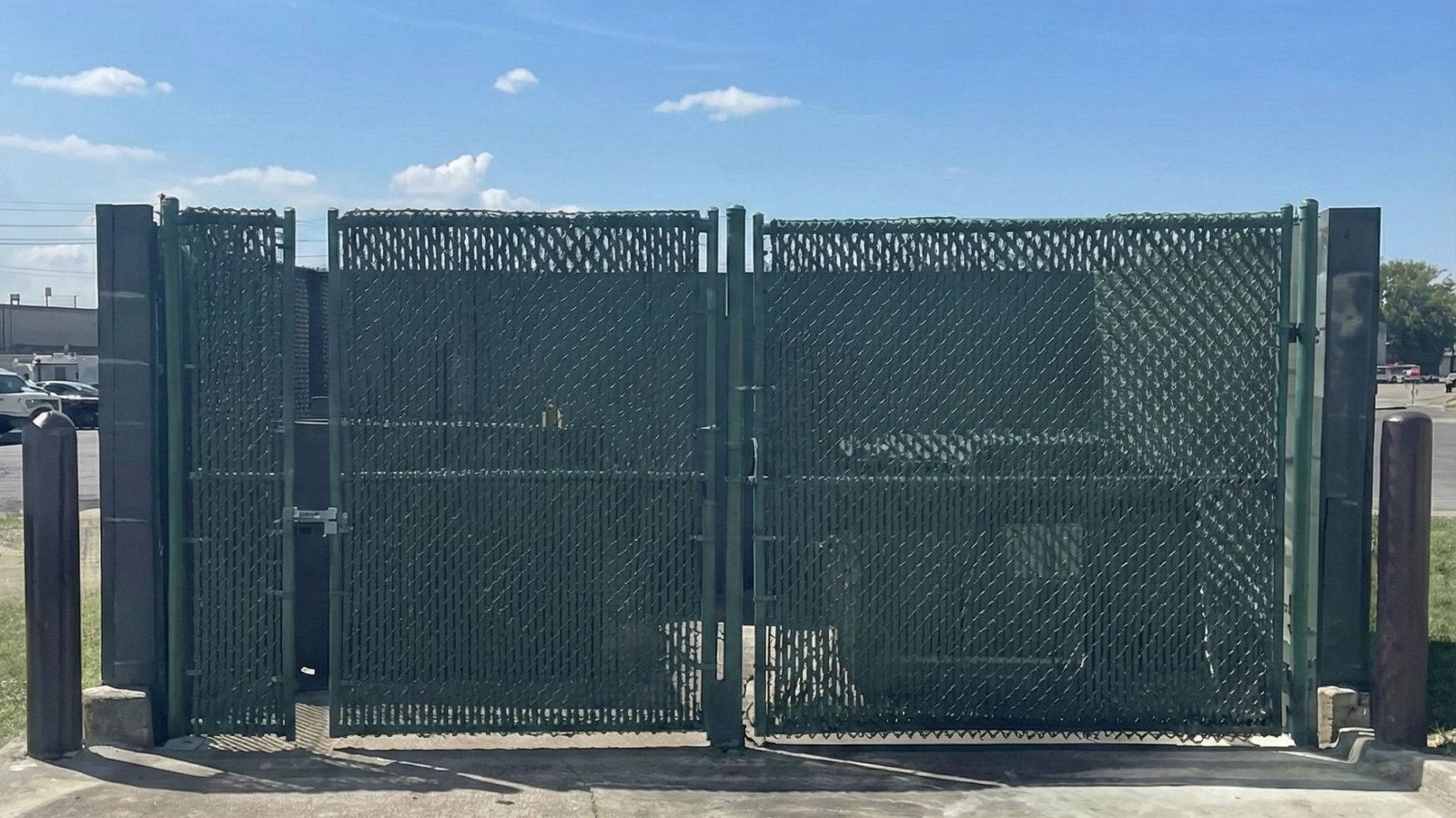 Green chain link industrial fence gate with privacy slats at commercial facility entrance on concrete pad