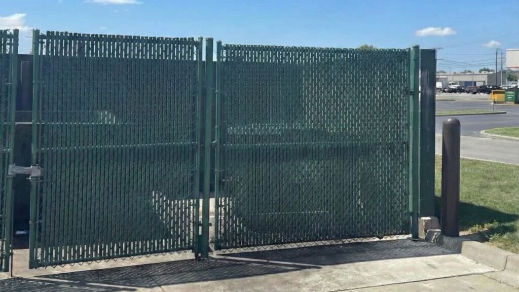 Green chain link industrial security gate with privacy slats installed at commercial facility entrance