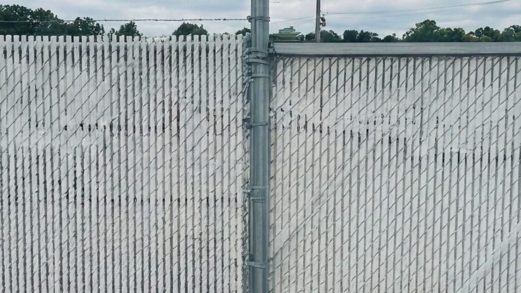 White chain link fence with privacy slats and barbed wire security features at commercial property