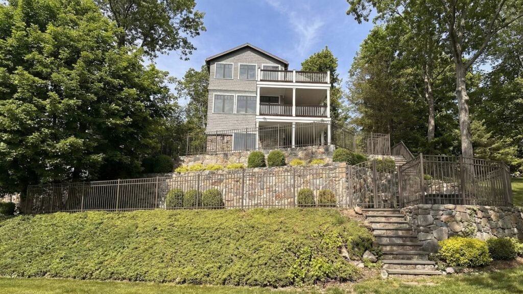 Three-story house with professional aluminum fencing installed on terraced stone retaining walls and landscaping