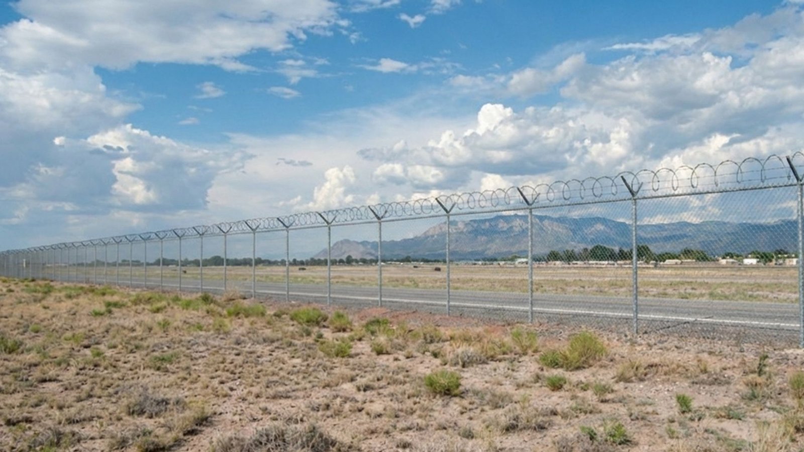 High security chain link fence with razor wire extending across arid landscape with mountains in background