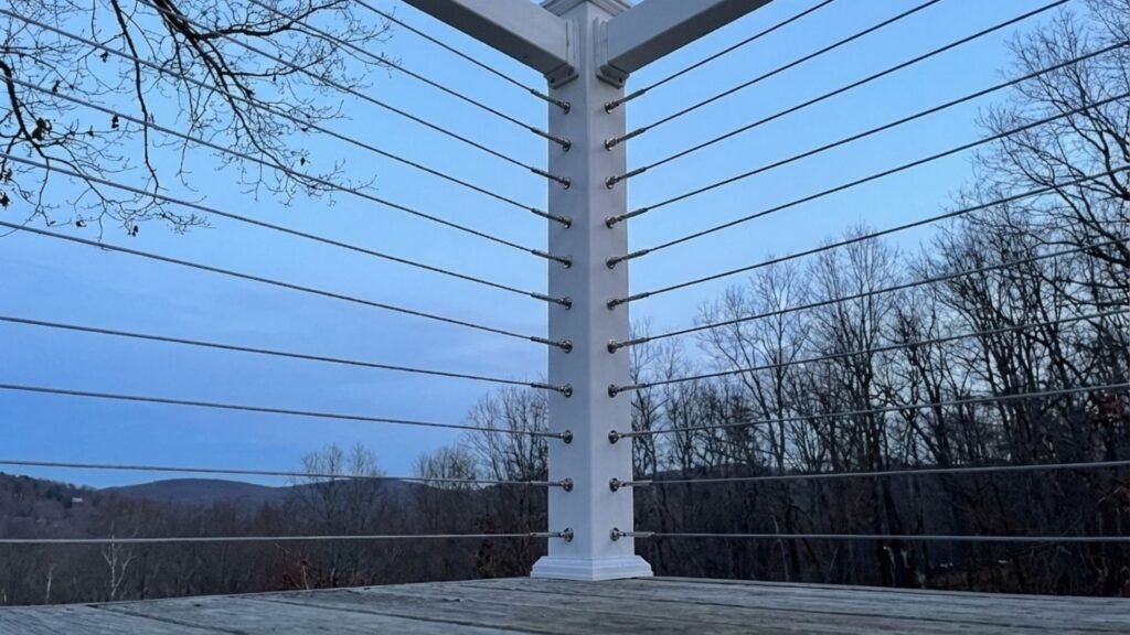 Modern white cable railing system with steel cables and white posts on wooden deck overlooking wooded hills