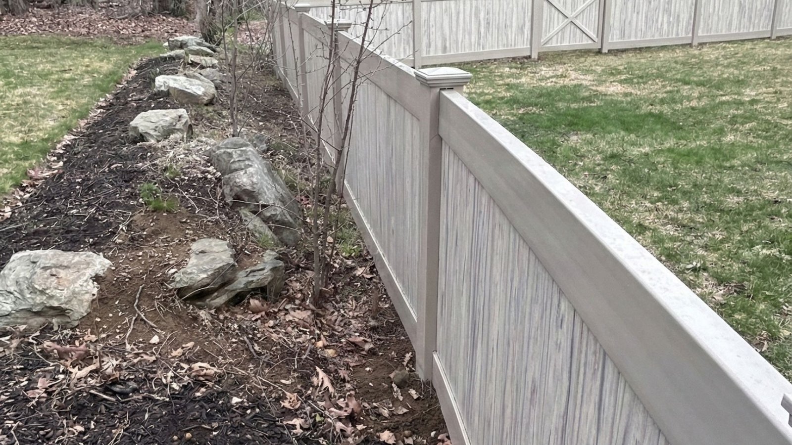 New beige vinyl privacy fence with horizontal slats installed along residential property line with landscaping