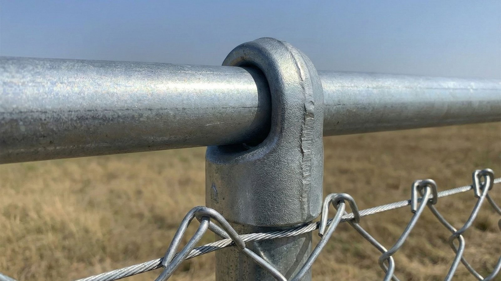 Close-up of galvanized chain link fence post and top rail connection with woven wire mesh fencing