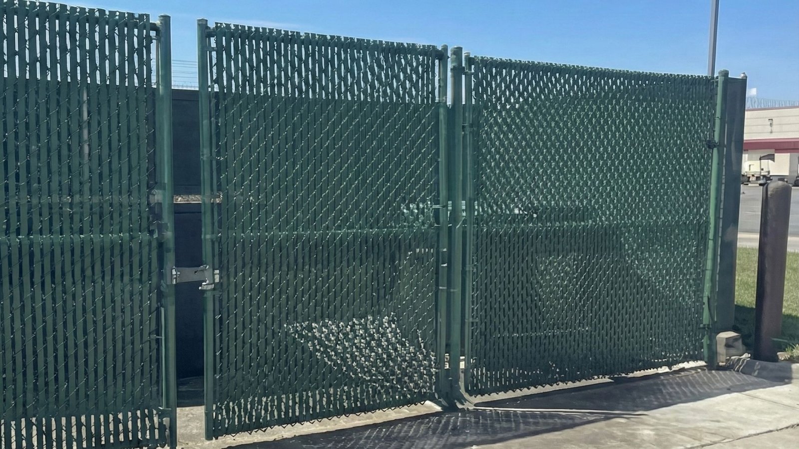 Green industrial chain link fence with privacy slats and security gate at commercial facility