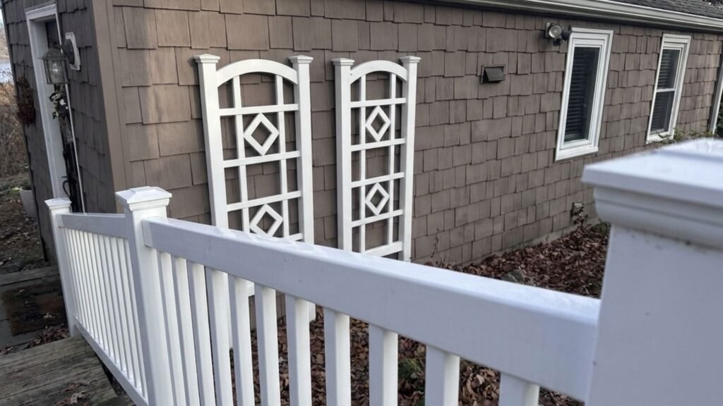 White decorative railing panels and fence posts installed next to brown shingled house exterior