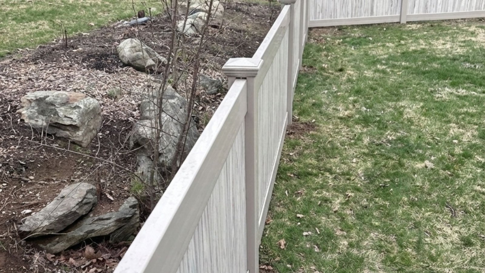 White vinyl privacy fence panels installed along property line with landscaping and bare trees in background
