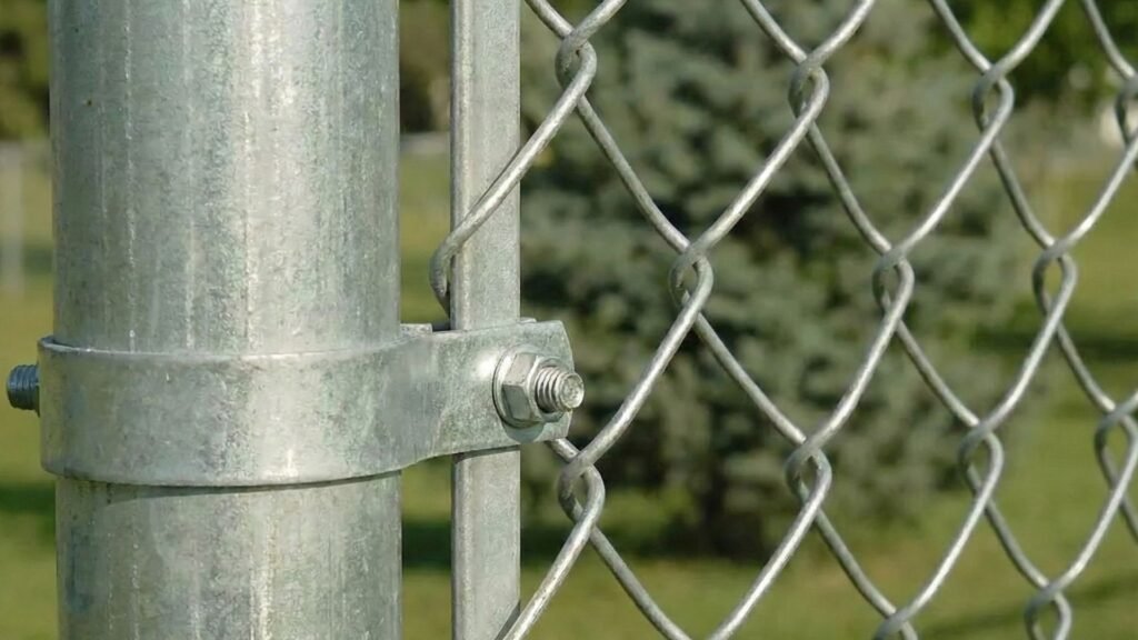Close-up view of galvanized chain link fence mesh attached to metal post with clamp hardware and bolt connection