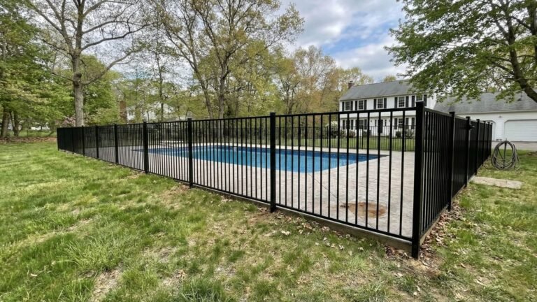 Wide backyard view of a completed aluminum pool fence surrounding an inground pool in Seymour CT with mature trees and a colonial-style home visible in the background